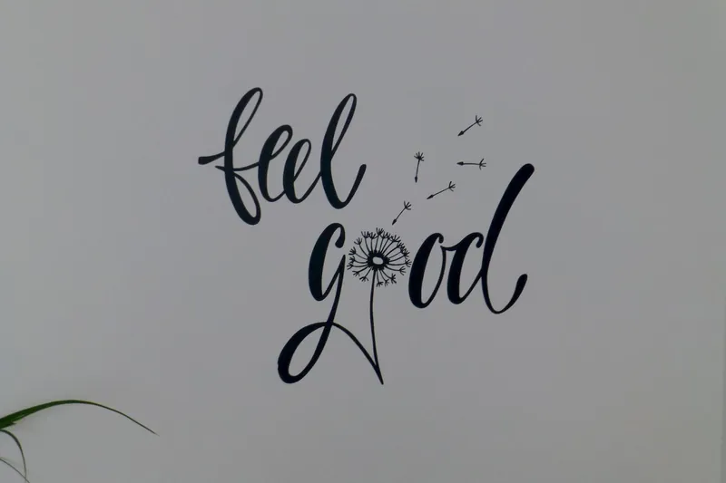 Handgeschriebener Schriftzug „feel good“ mit Pusteblume an einer hellen Wand
