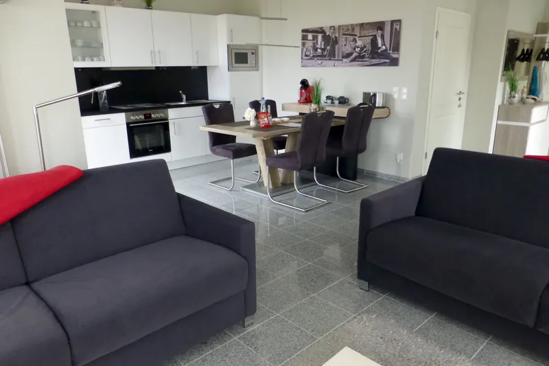 Sofaecke im Vordergrund, dahinter die weiße offene Küche mit Esstisch