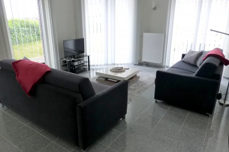 Zwei Sofas mit roten Decken, Flachbild-Fernseher und Terrassentür zum Garten