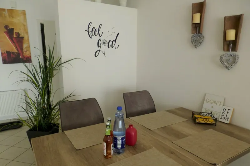 Esstisch mit Stühlen vor einer Wand mit „feel good“-Schriftzug