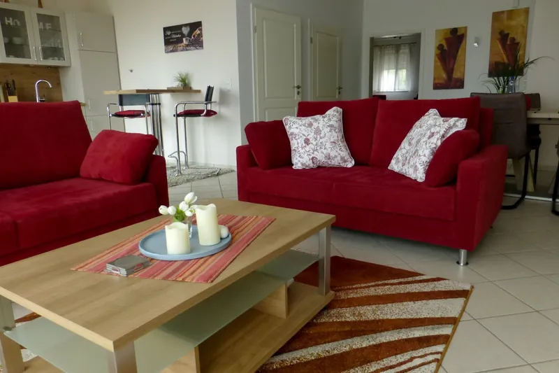 Wohnbereich von Fördeblick 2 mit roten Sofas und raumhohen Fenstern zum Garten und zur Ostsee