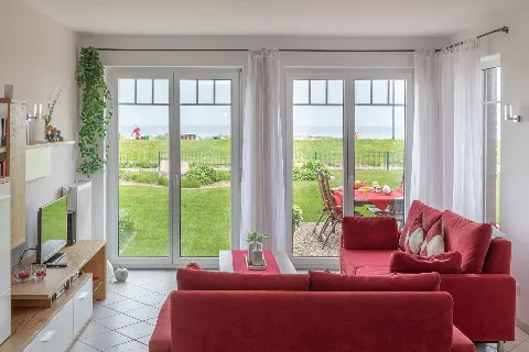 Rote Sofas vor zwei Terrassentüren mit Blick auf Garten und Deich