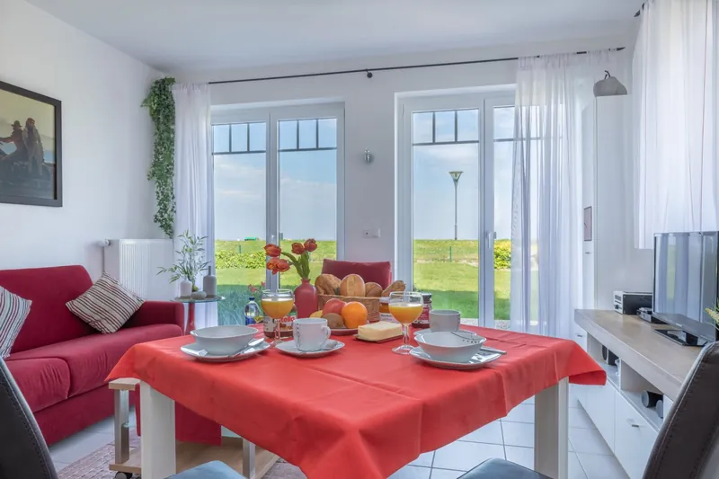 Gedeckter Frühstückstisch in Fördeblick 3, dahinter Terrassentüren mit Blick über den Deich zur Ostsee