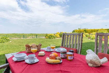 Gedeckter Frühstückstisch mit roter Decke auf der Terrasse, dahinter der Deich