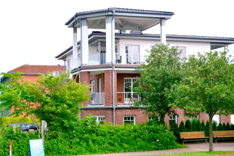 Klinkerhaus mit weißem Eckturm und Balkonen hinter Bäumen