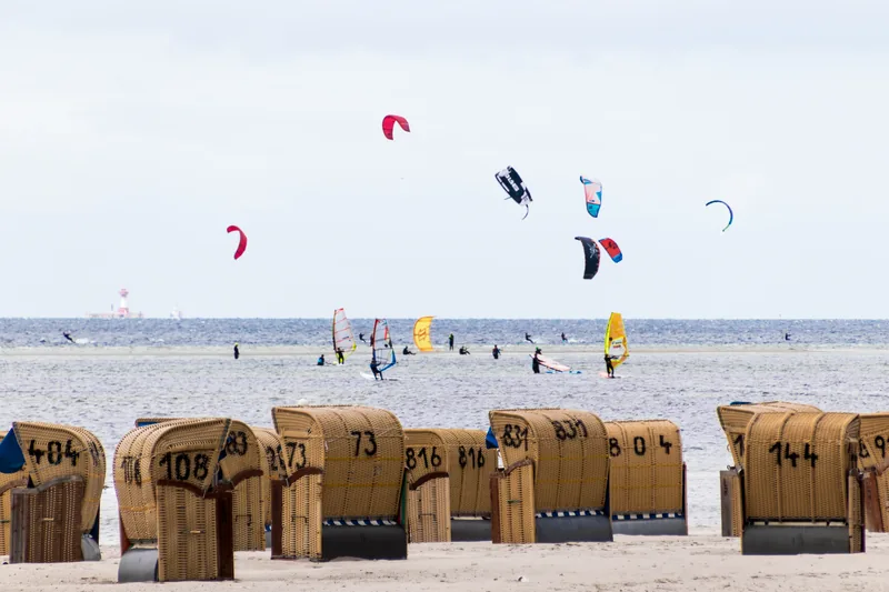 Kite- und Windsurfer auf der Ostsee bei Laboe, im Vordergrund eine Reihe nummerierter Strandkörbe