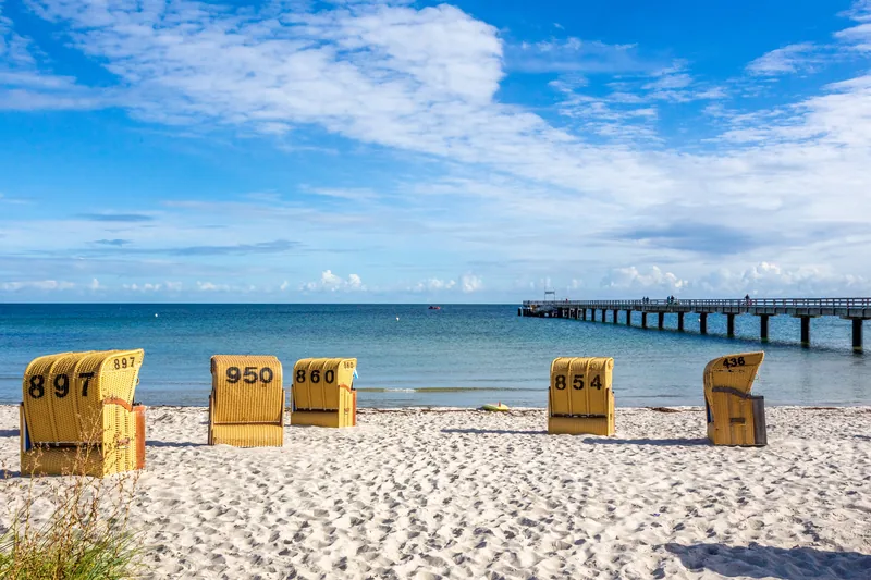 Gelbe Strandkörbe auf dem hellen Sandstrand von Schönberger Strand, rechts die Seebrücke in der Ostsee