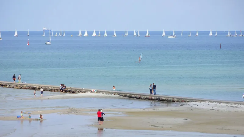 Spaziergänger auf der Mole, am Horizont viele Segelboote einer Regatta
