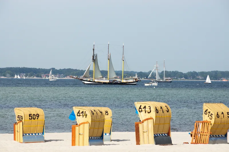 Dreimast-Segelschiff vor der Küste von Laboe, im Vordergrund nummerierte Strandkörbe auf dem Sand